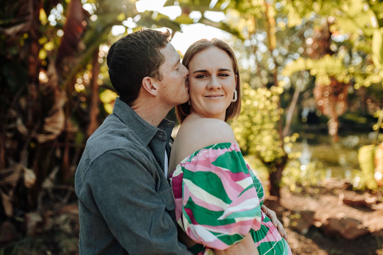 Romantic couple shares tender moments in golden sunlight while wearing casual attire in an outdoor setting.