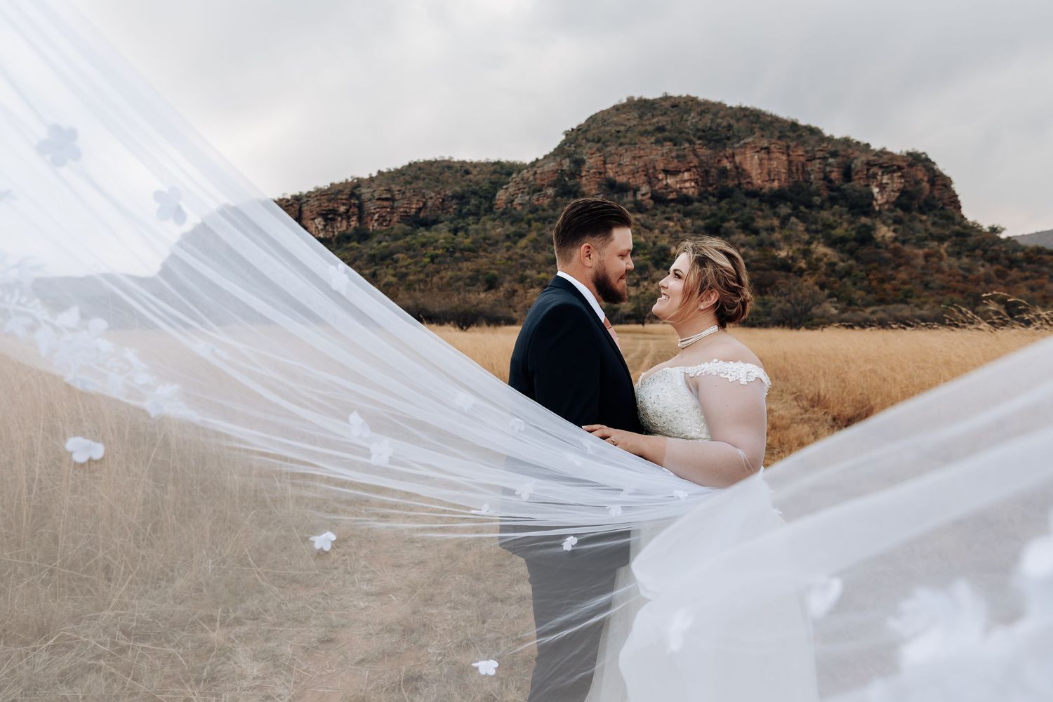 Scenic desert mountain backdrop with flowing white wedding veil trailing in the wind during a romantic moment.