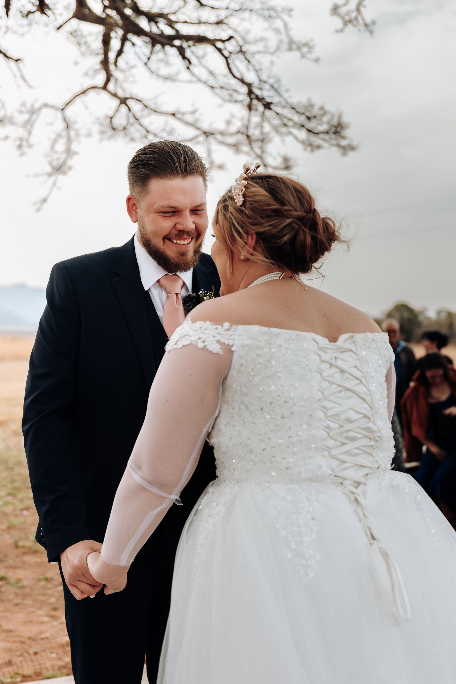 A bride and groom share a joyful moment during their outdoor wedding ceremony under a rustic tree branch.