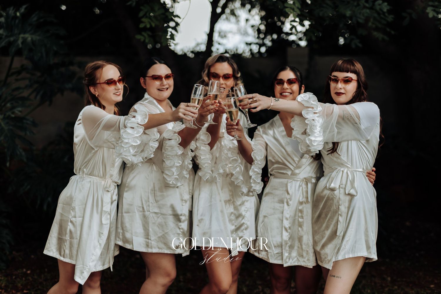 Bridesmaids in matching white satin robes posing together.