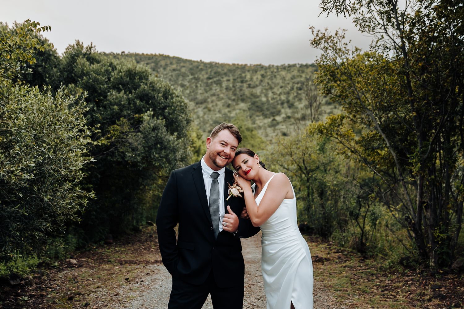 A couple shares romantic moments along a wooded mountain path on their wedding day.