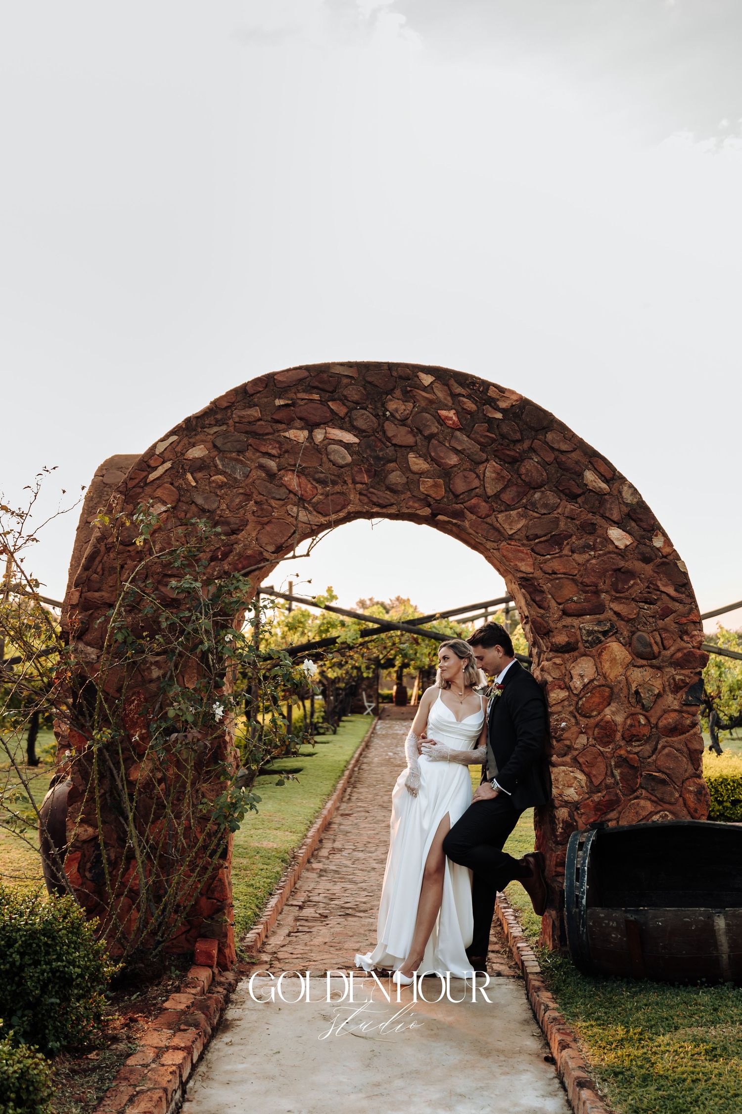 Wedding couple shares intimate moments under a rustic stone archway at sunset.