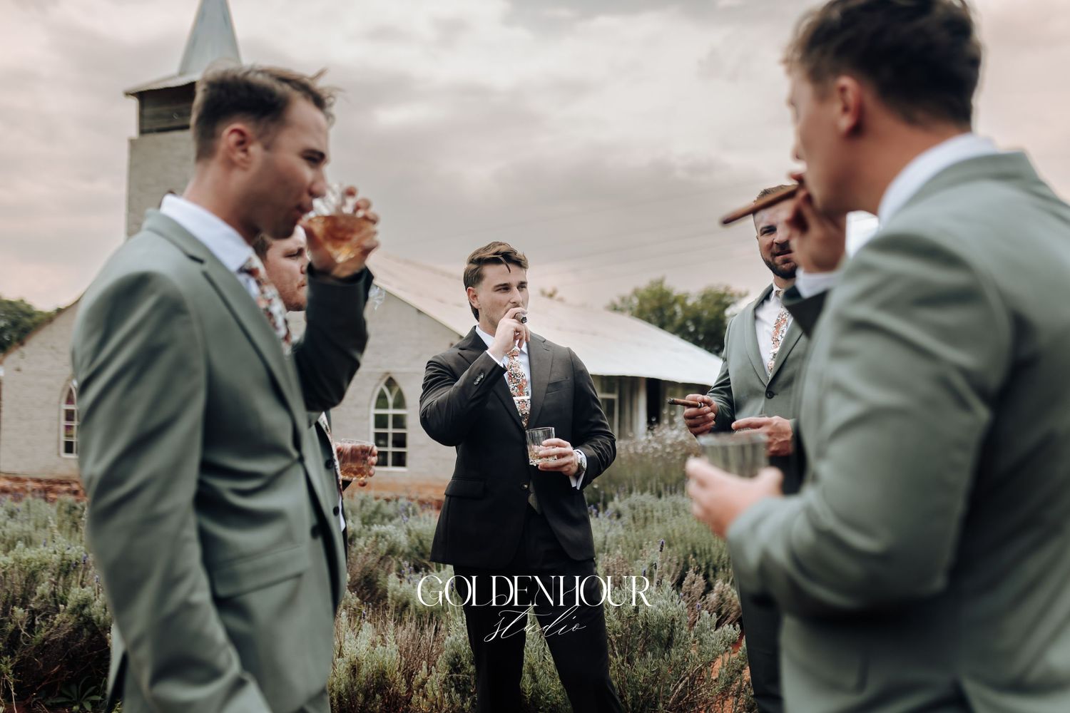 Wedding party wearing sage green suits gather together in a garden setting during a celebration.