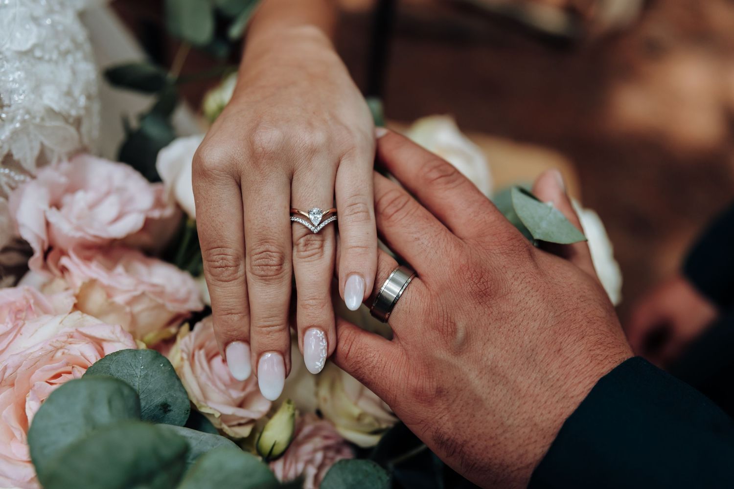 Close-up detail shots of hands holding delicate pink roses and wedding rings during a romantic ceremony.