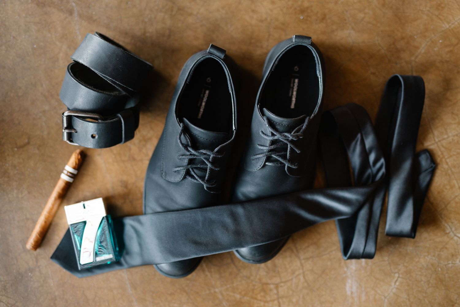 Black leather boots and accessories arranged in a line on brown textured background.
