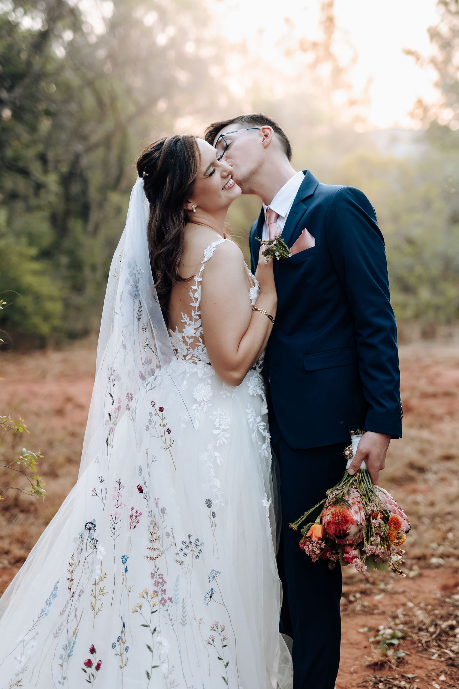 A romantic wedding photo series showing a couple embracing in a misty forest setting with a flowing white veil and navy suit.