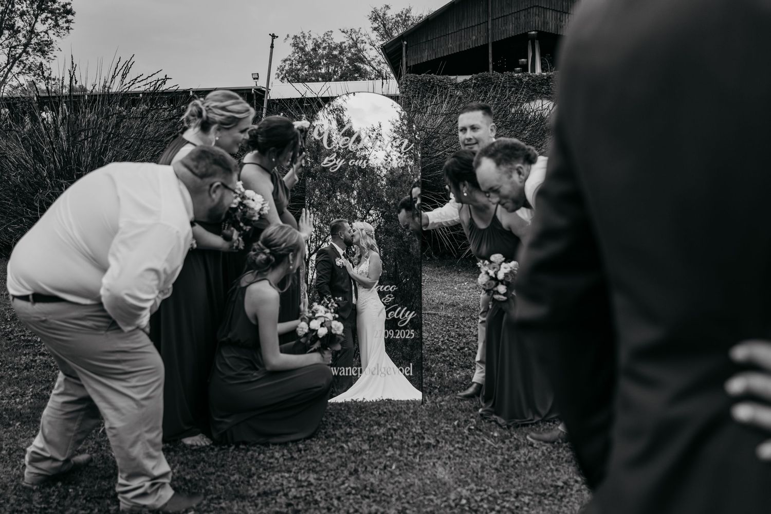 Black and white photo of wedding guests bending down to look at something in an outdoor garden setting.