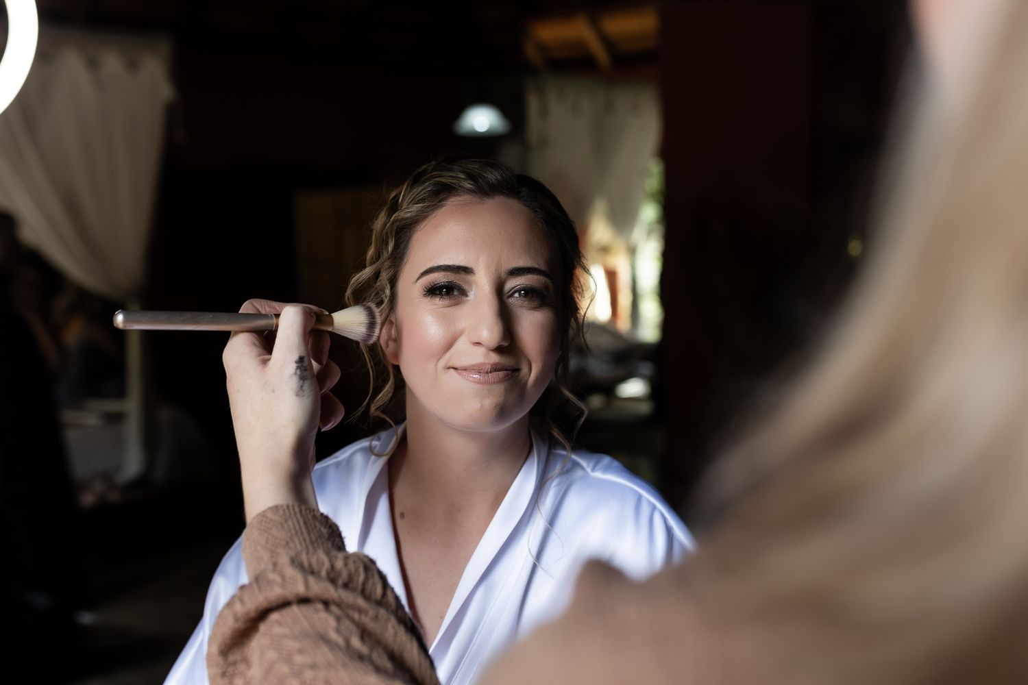 Getting ready scene with makeup being applied to someone in a white robe.