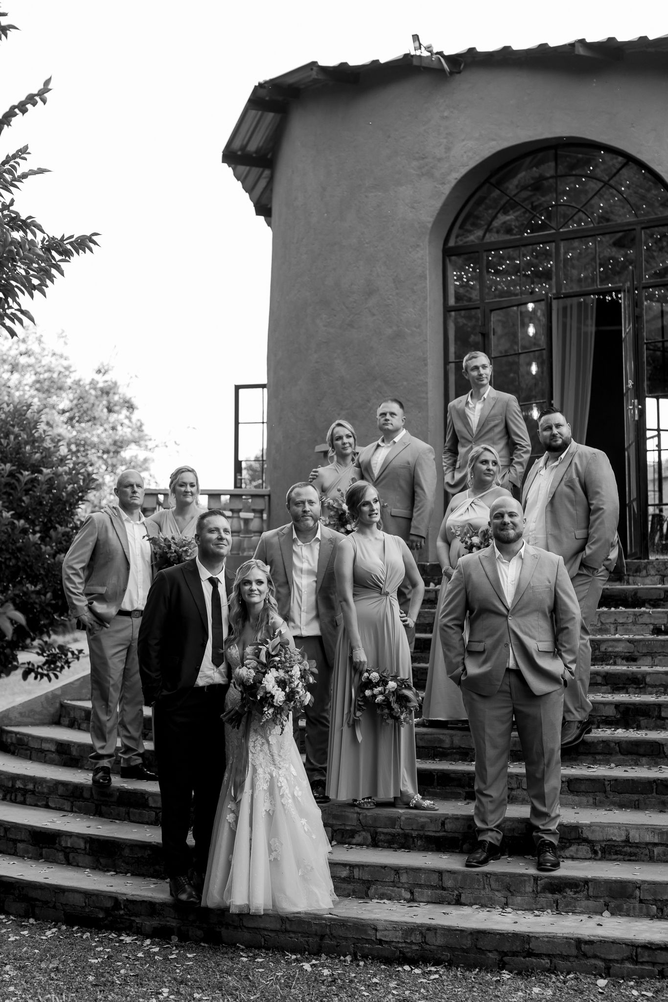 Wedding party gathered on stone steps of historic building in black and white photograph.