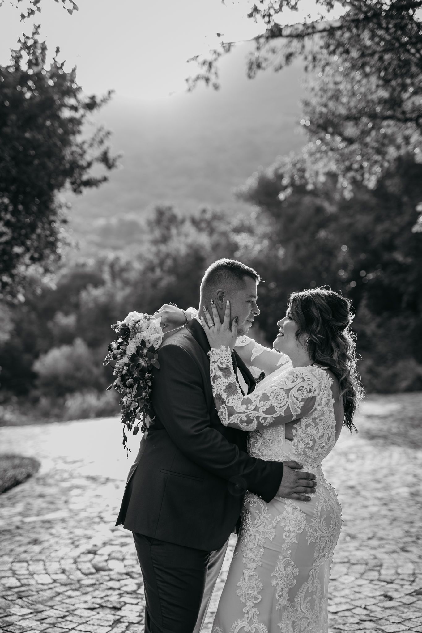 Romantic black and white portrait of bride and groom embracing on stone path.