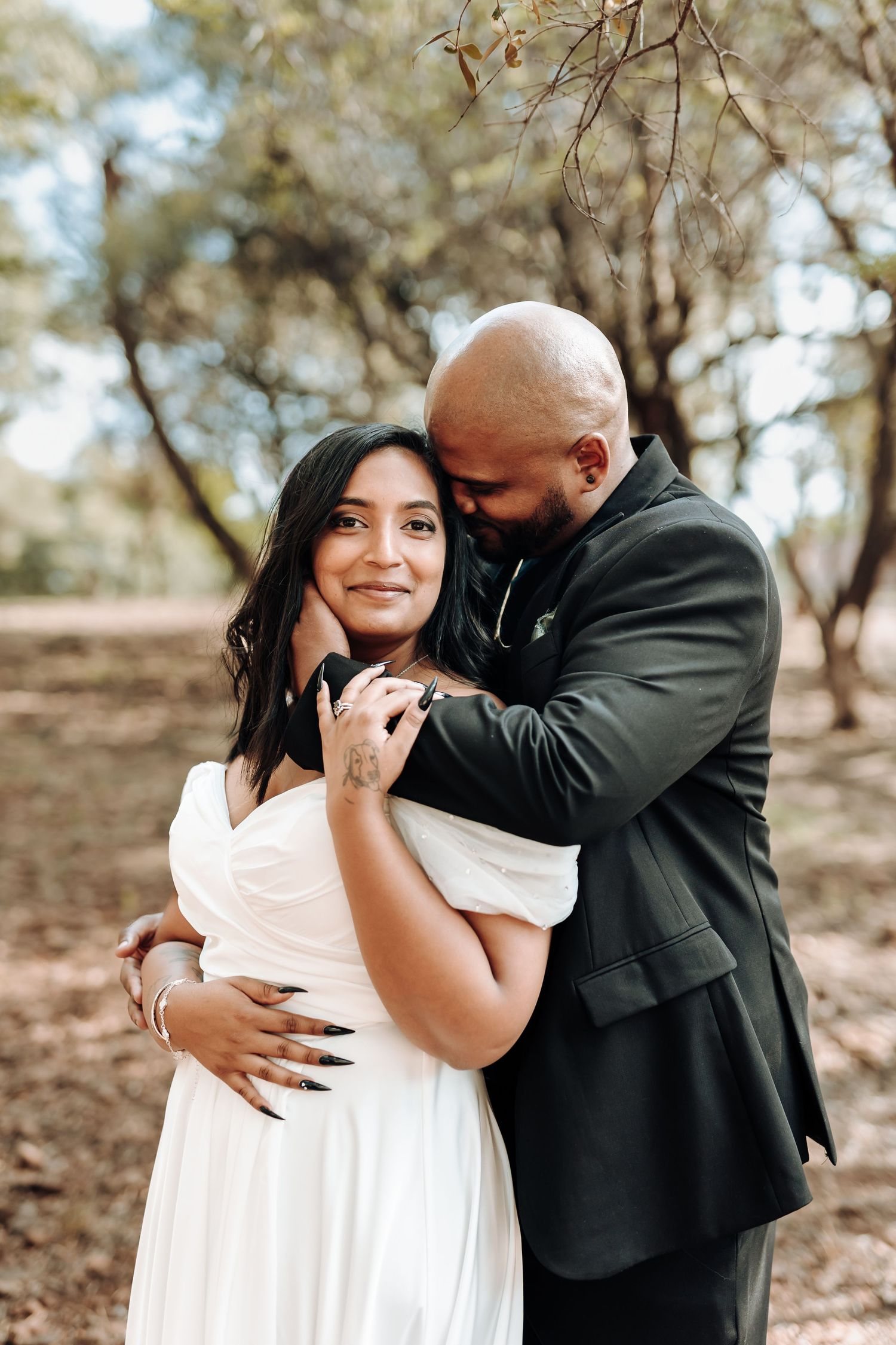 A romantic couple share an intimate moment during their wedding photoshoot in a wooded area.