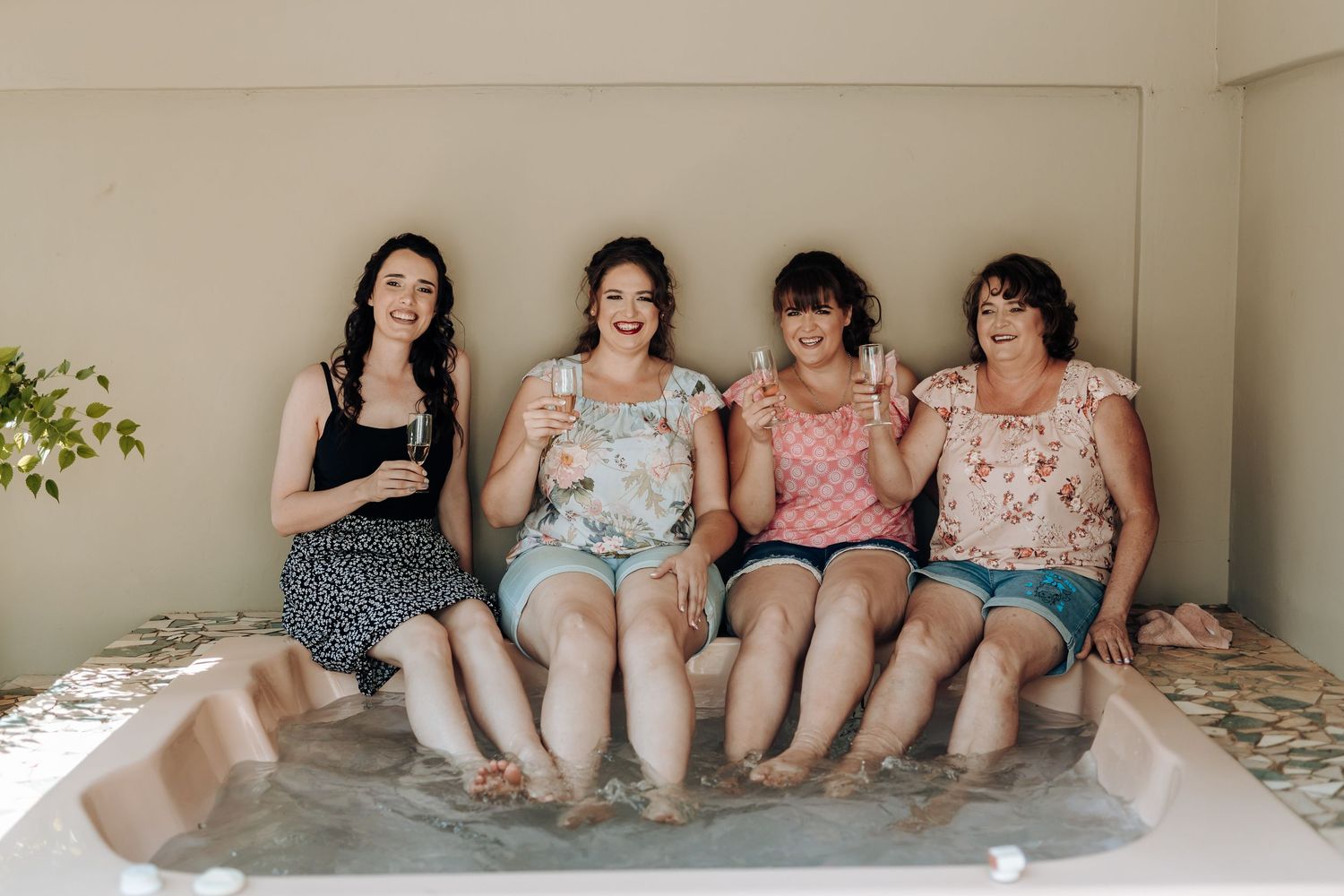 Group sitting side by side with feet in water, sharing drinks and conversation.