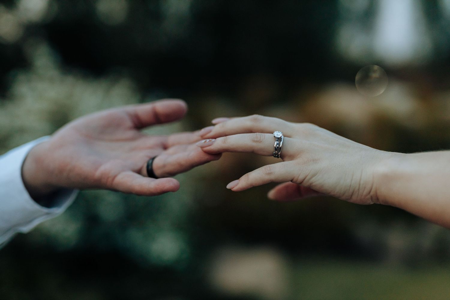 Close up of hands exchanging wedding rings with soft focus nature background.