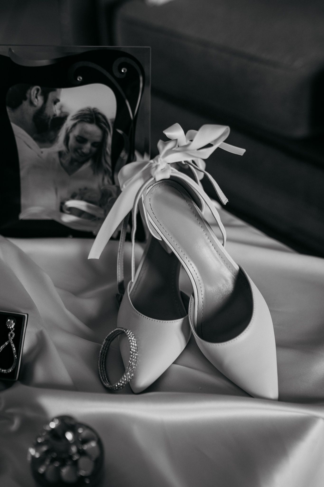 Elegant white bridal shoes with bow detail next to vintage photograph on silk fabric.