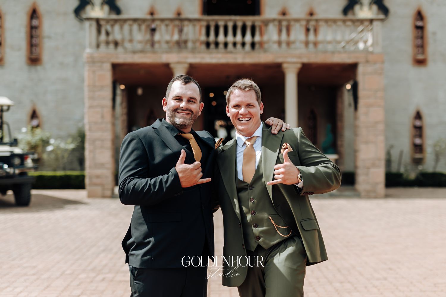 Two grooms smiling and giving thumbs up outside beautiful wedding venue.