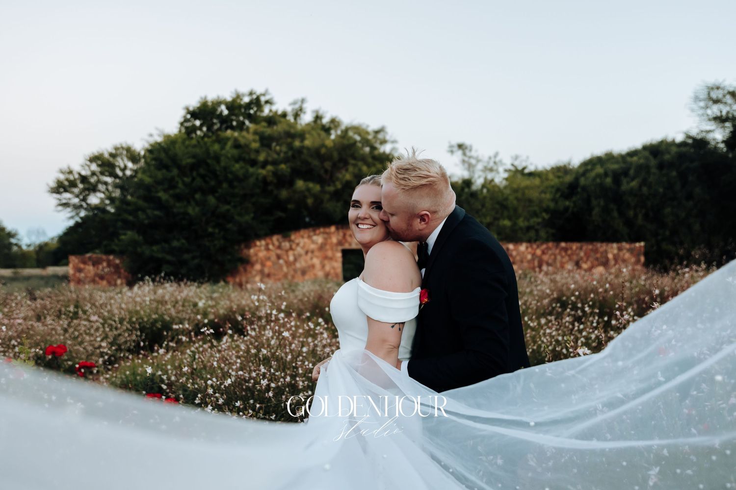 A couple embraces in a cotton field during sunset while a long white veil flows in the breeze.