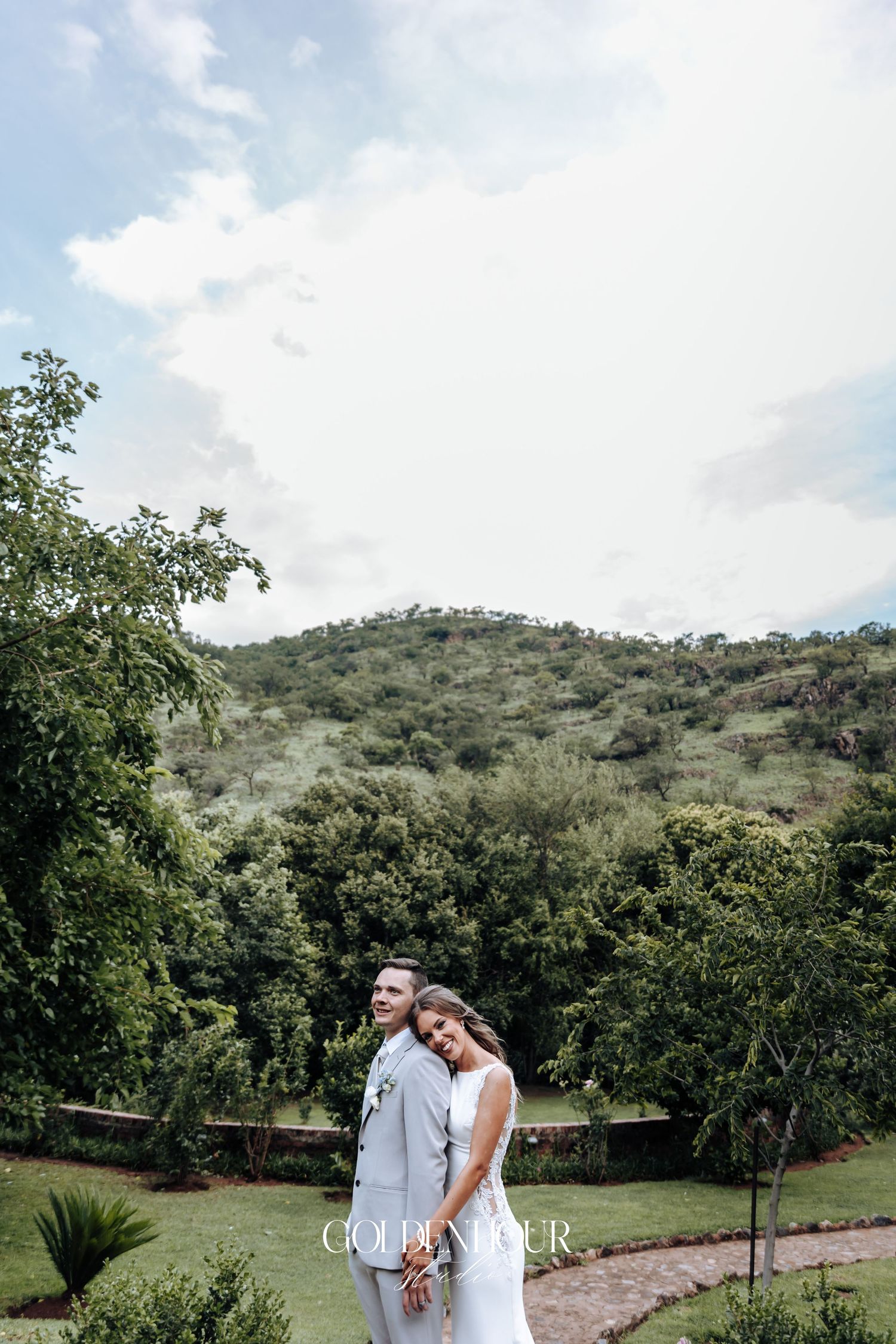 Newlyweds share a romantic moment in a scenic mountain landscape with lush greenery.