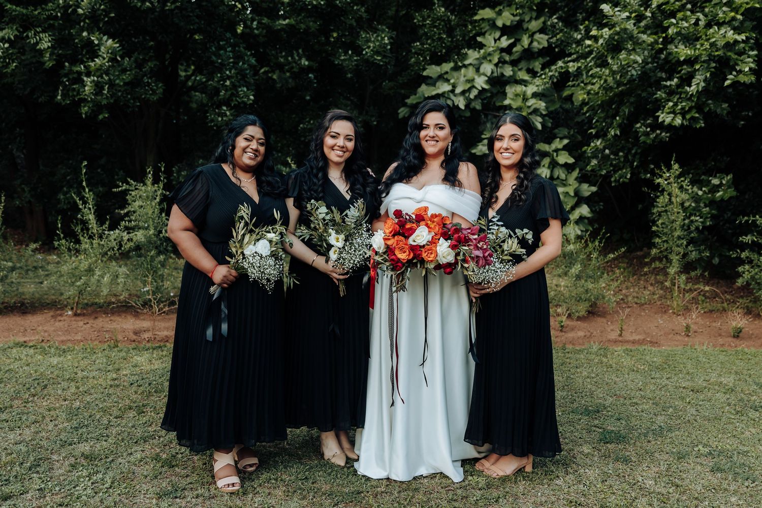 Wedding party in black and white attire poses outdoors with floral bouquets.