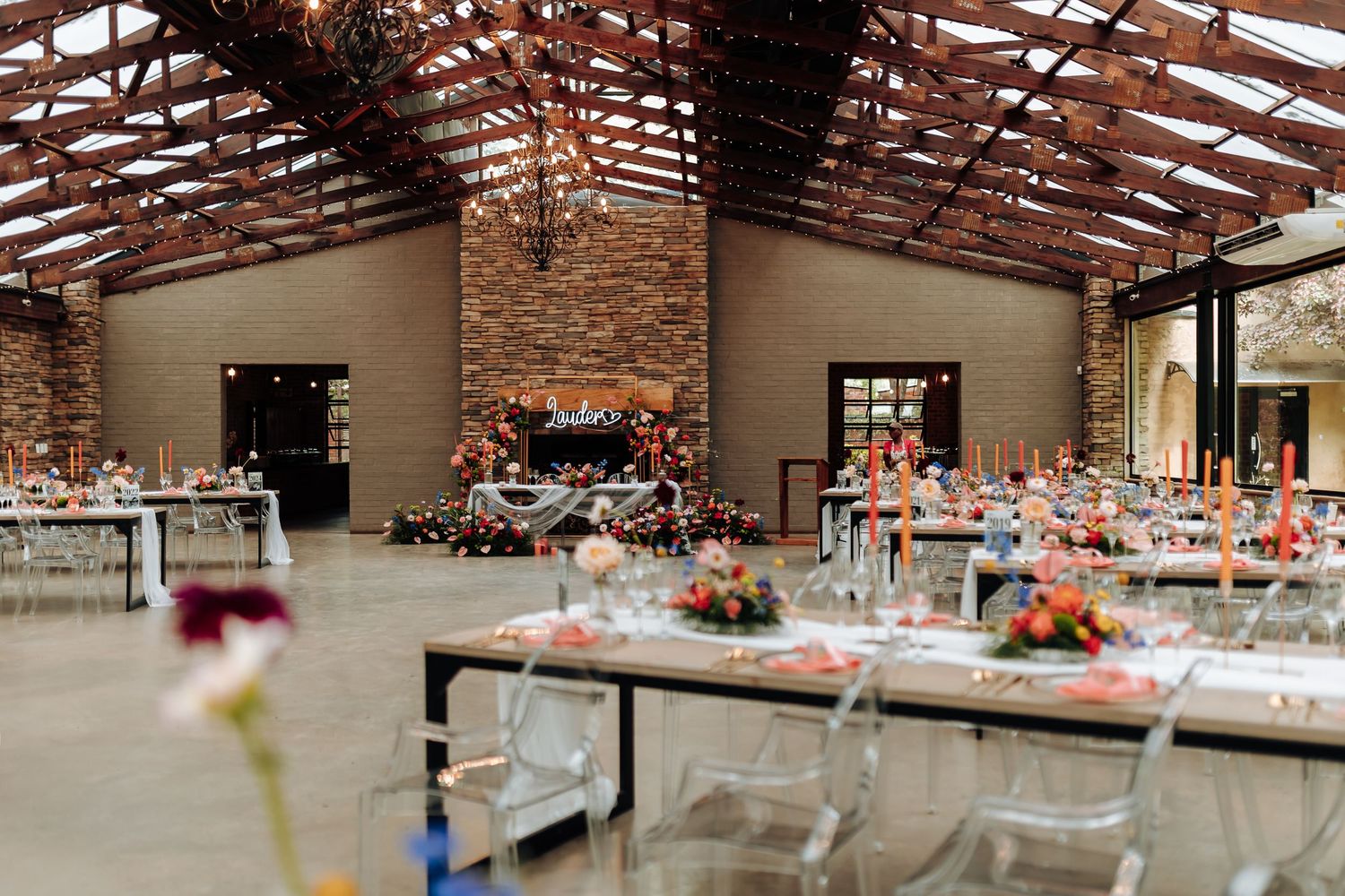 Rustic wedding reception venue with exposed wooden beams, brick walls, and elegant table settings decorated in coral tones.