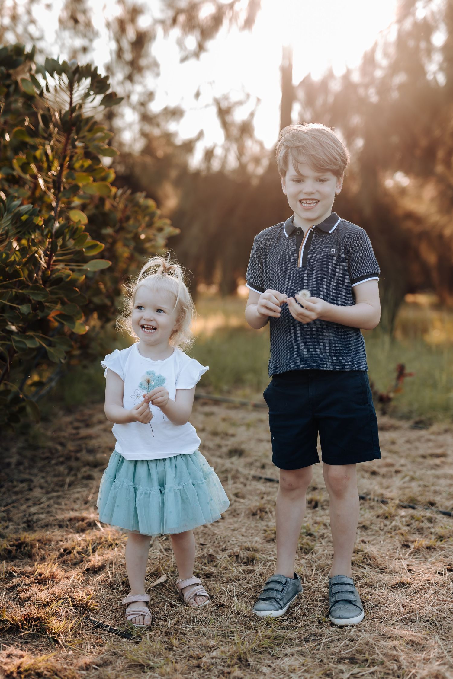 Young siblings share a sweet moment together in the golden sunlight as they stand together in nature.