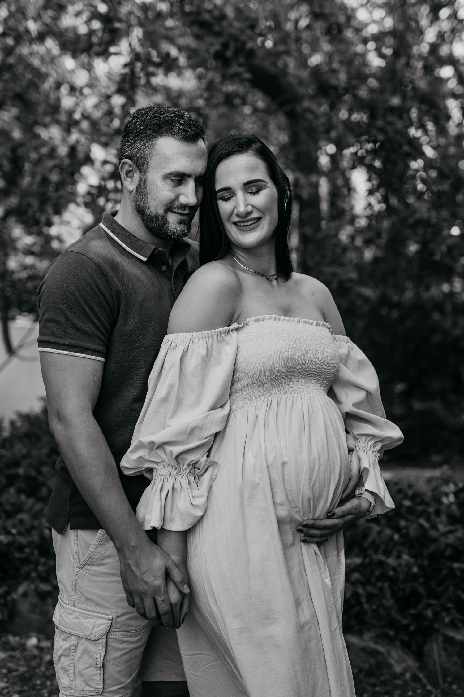 Black and white outdoor maternity photos showing couple in romantic poses among trees.