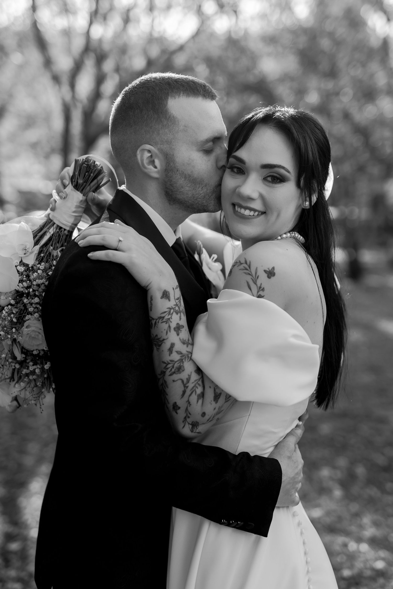 A black and white wedding photo shows a joyful moment between newlyweds as they embrace outdoors.