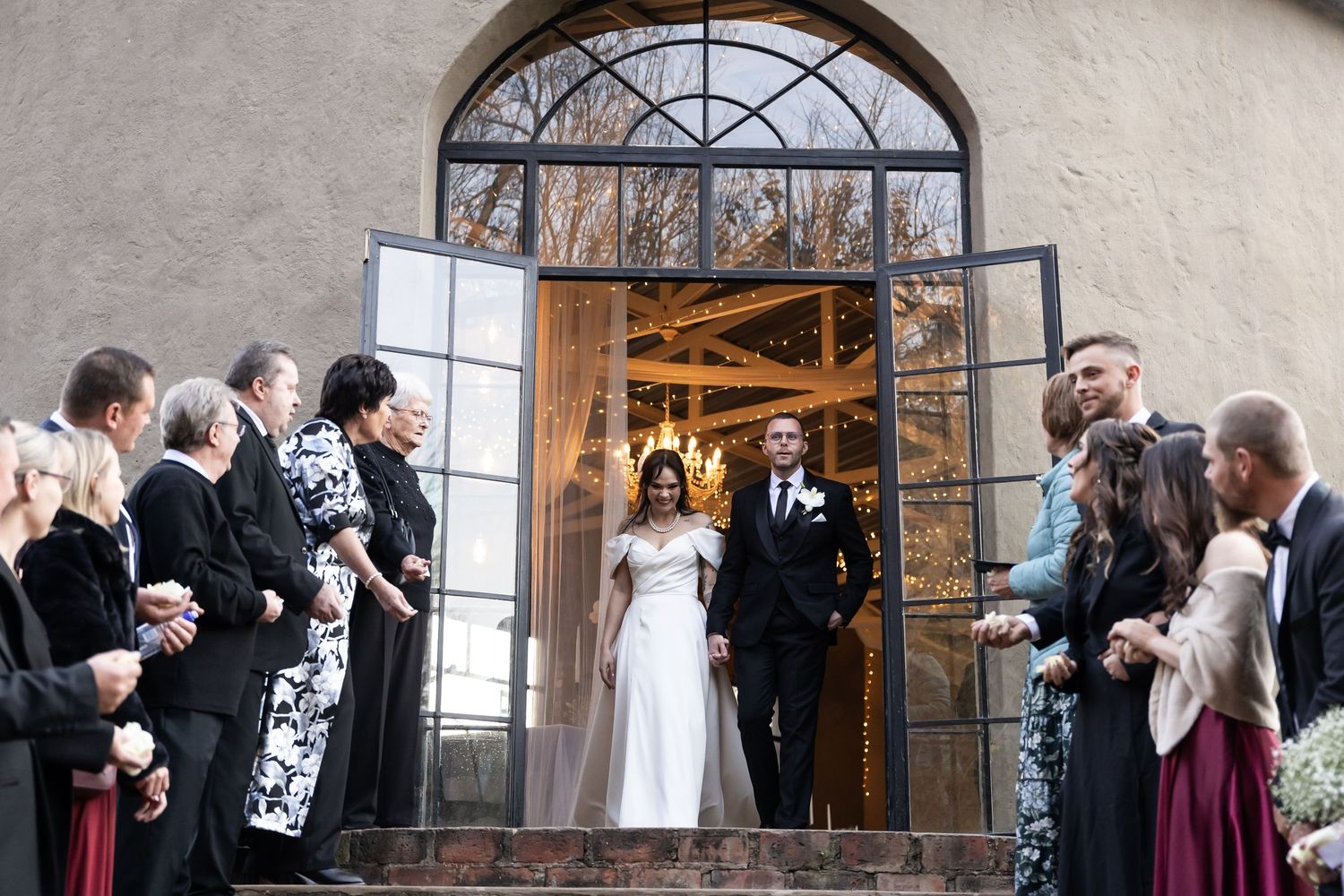Guests line both sides of a church entrance throwing confetti as newlyweds emerge from arched doorway.