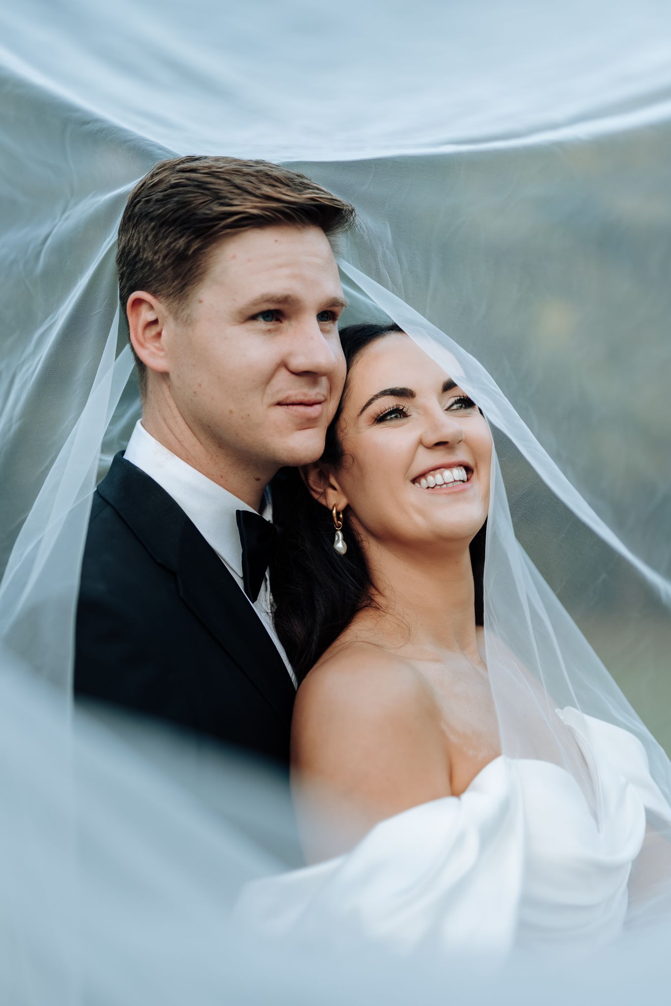 A tender wedding portrait framed by flowing white tulle veil.