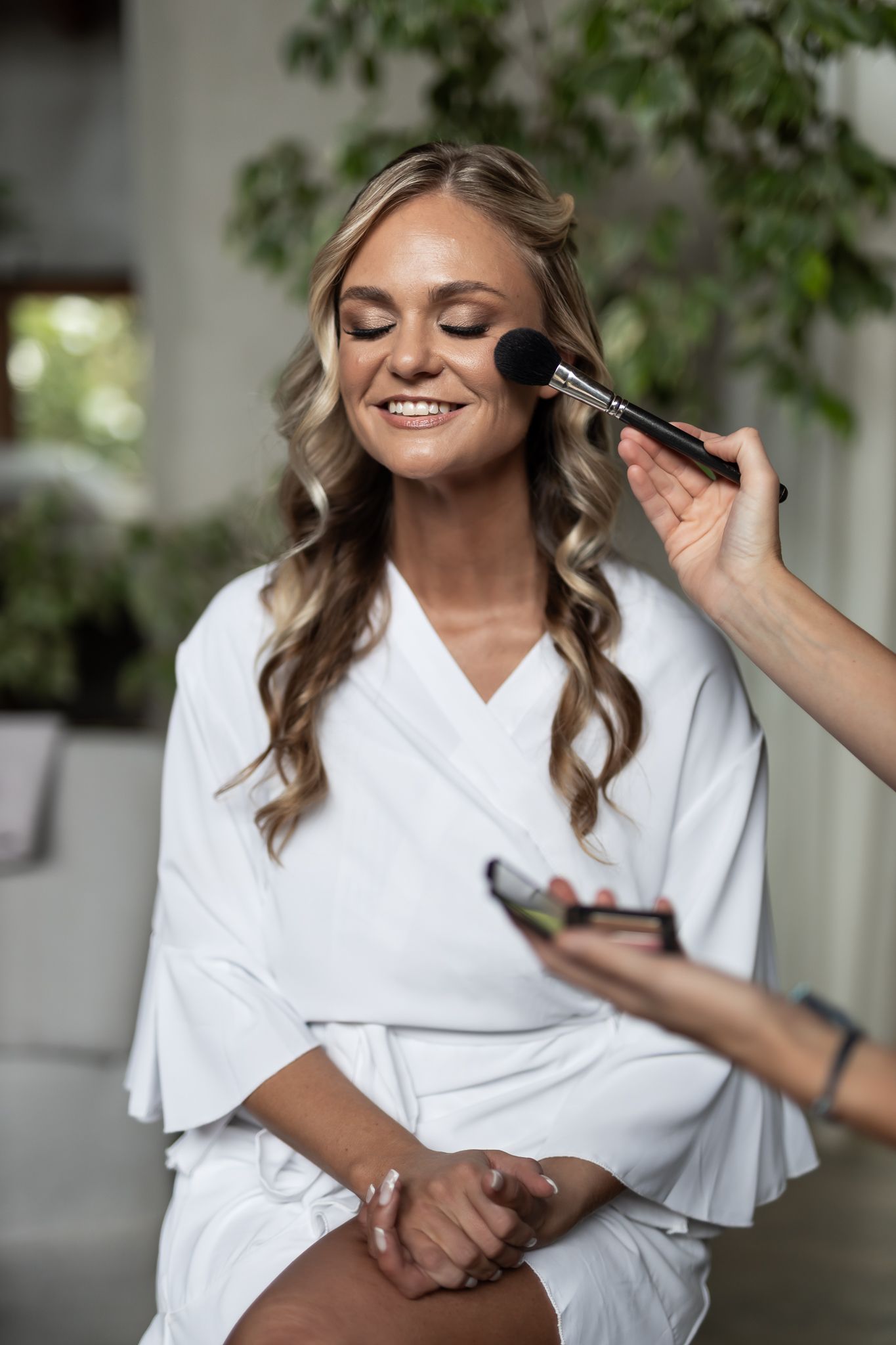 A makeup artist applies cosmetics during bridal preparations in a bright indoor setting.