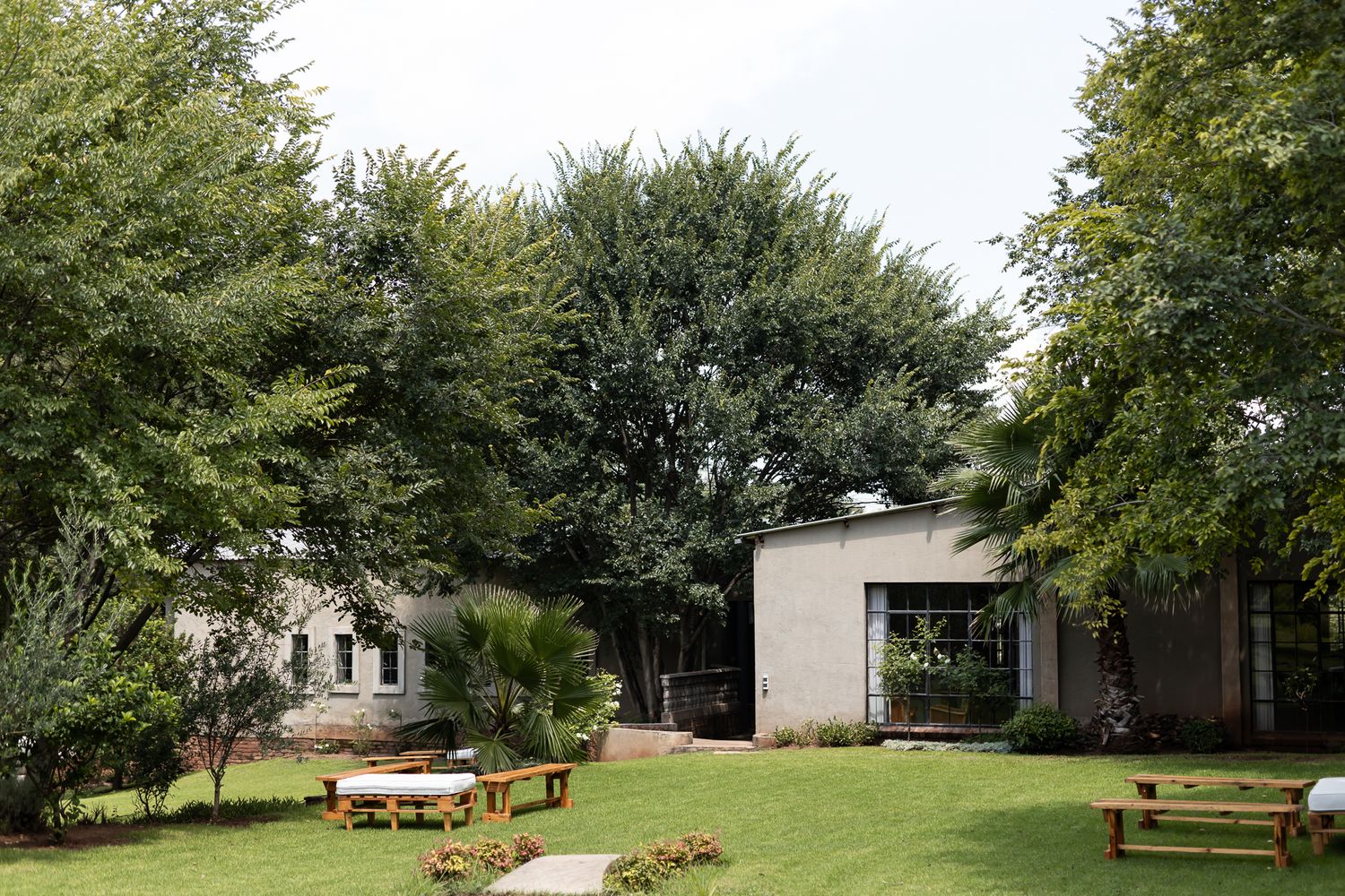 Modern building exterior with picnic tables on a lush green lawn surrounded by mature trees.
