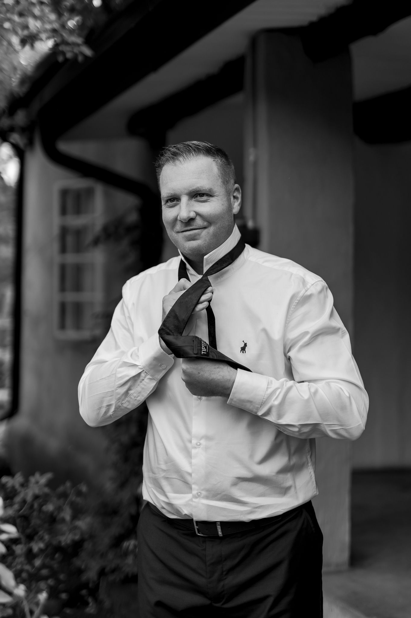 Person in white dress shirt adjusting navy tie in black and white portrait.