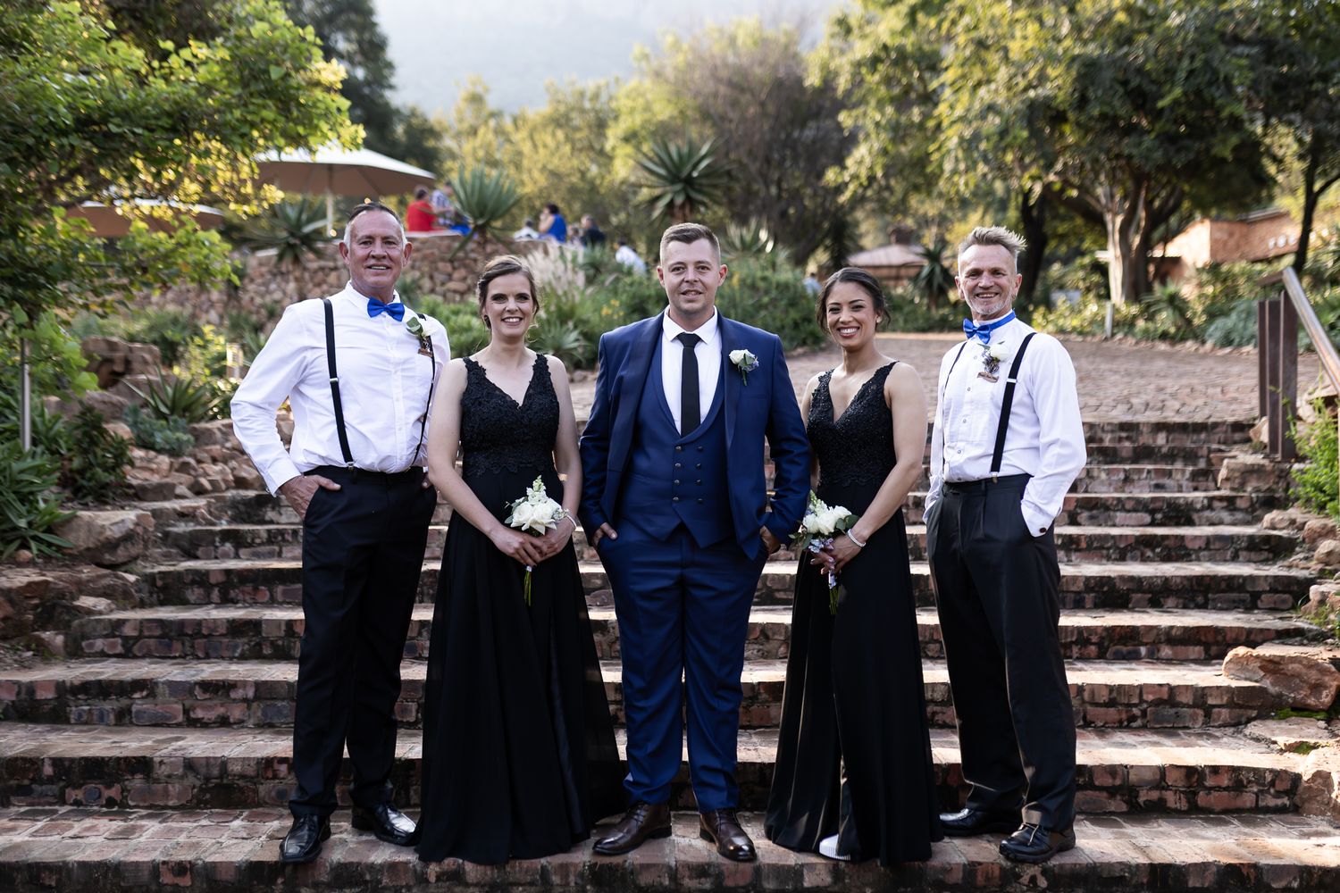 Wedding party in formal attire poses on rustic stone steps.