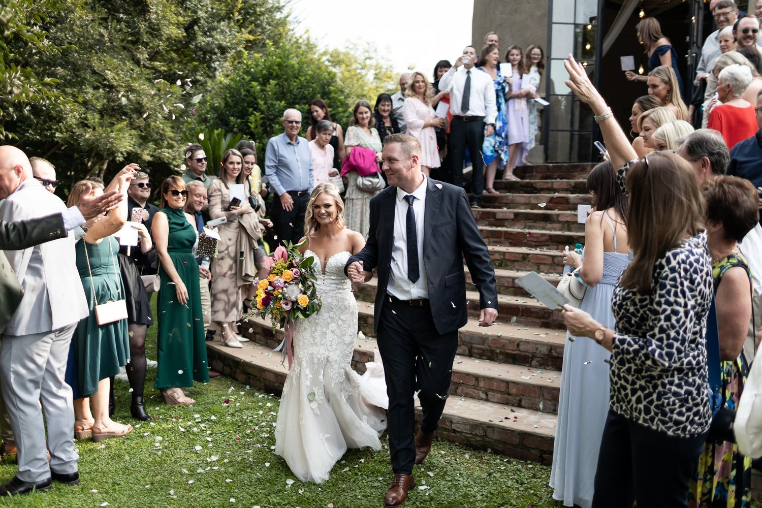 Wedding party exits church while guests line the steps throwing celebratory confetti.