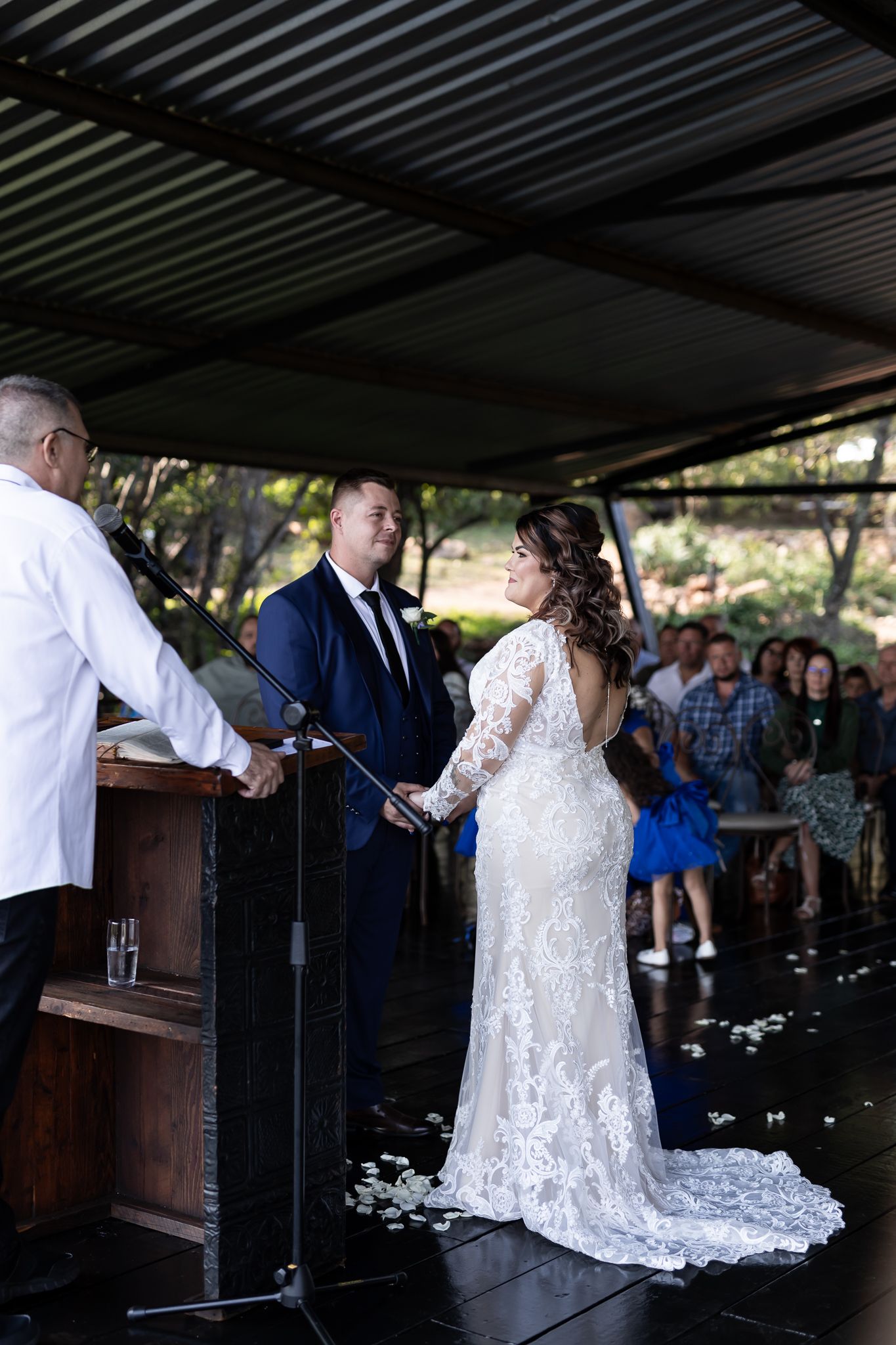 Wedding ceremony under covered outdoor pavilion with bride in detailed lace gown.