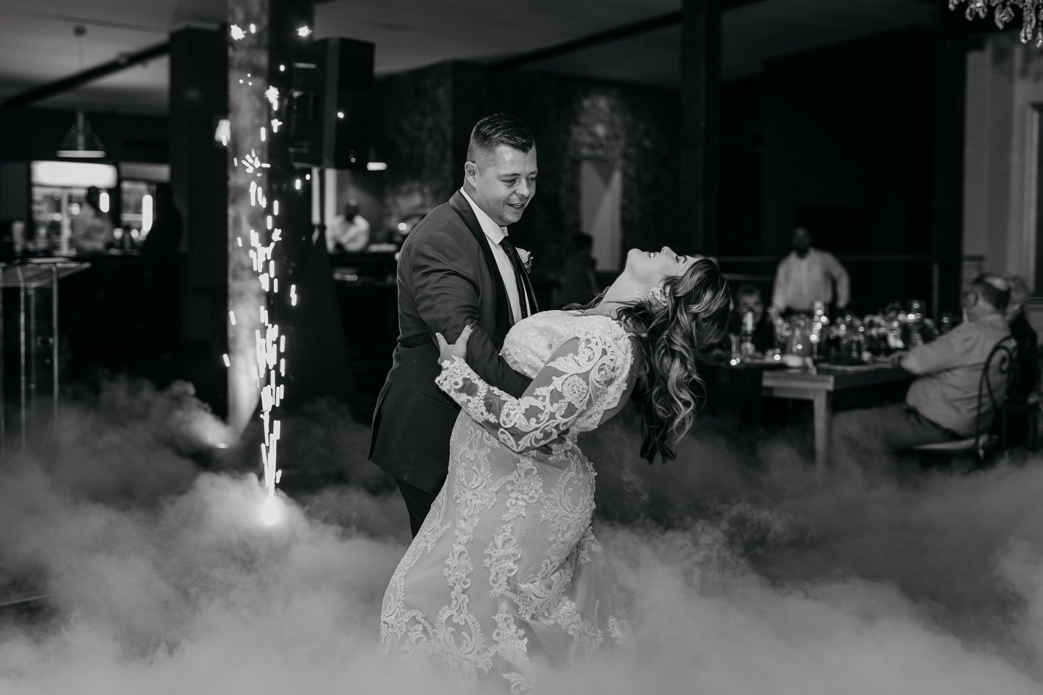 Black and white capture of wedding couple dancing amid atmospheric fog and sparklers.