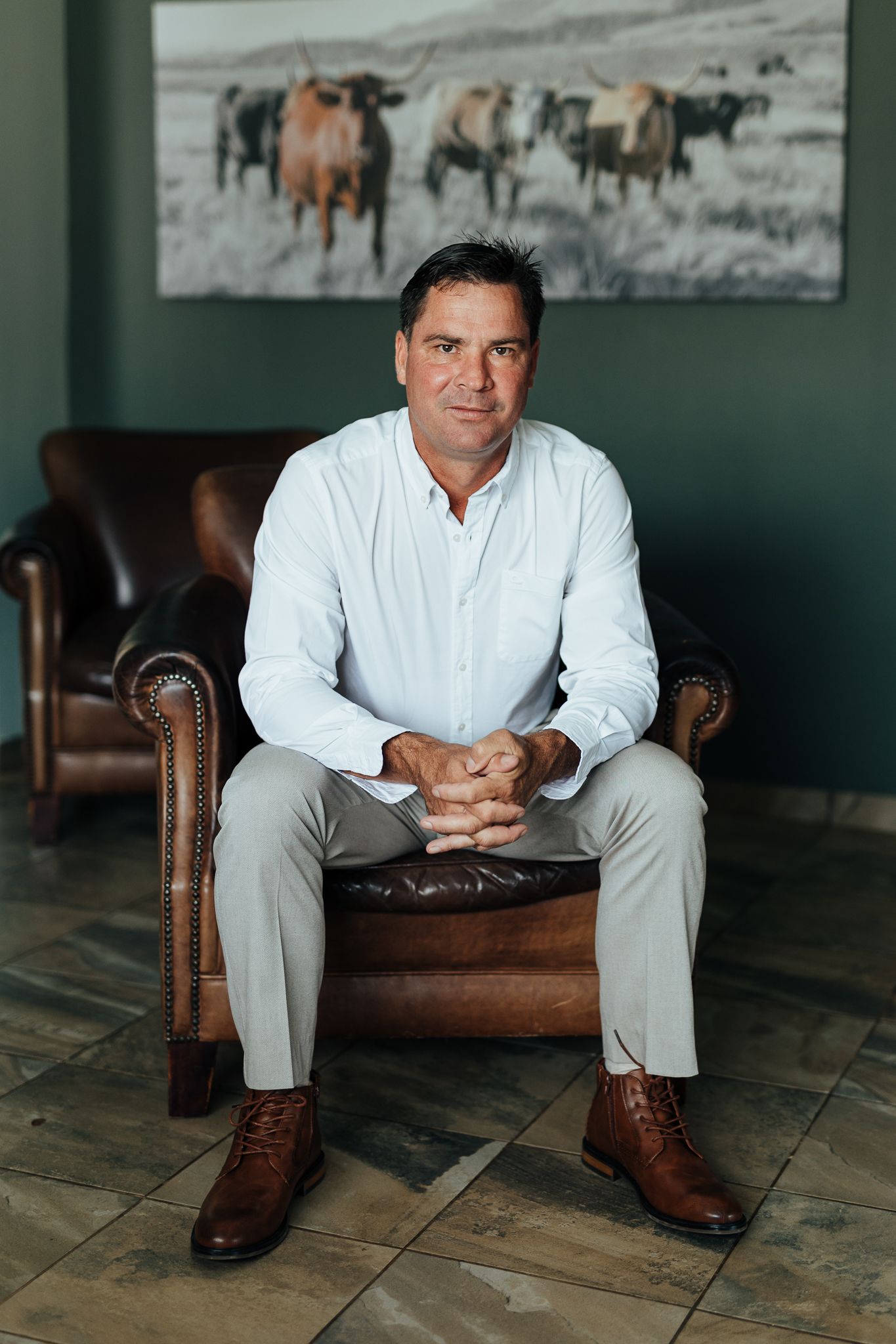 Formal portrait in a room with leather chair and horse artwork featuring white shirt and khaki pants.