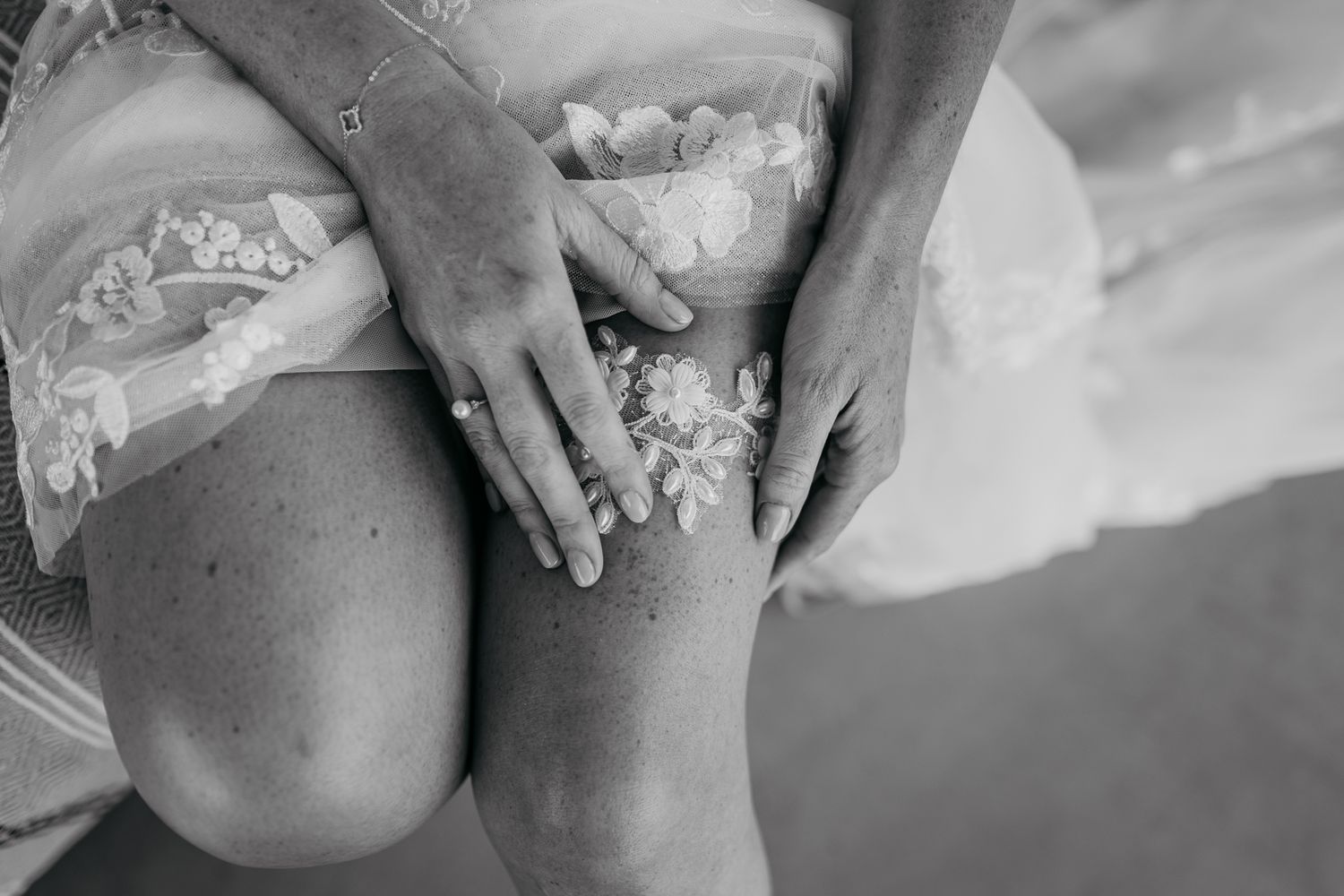 Close-up detail shot of hands resting on lace wedding dress fabric.