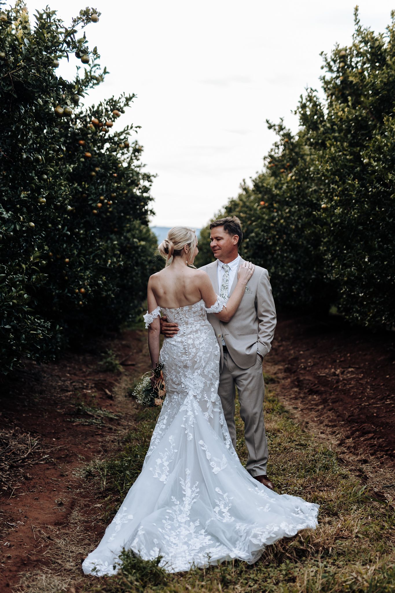 Romantic wedding portrait in an orchard with detailed lace dress and light beige suit.