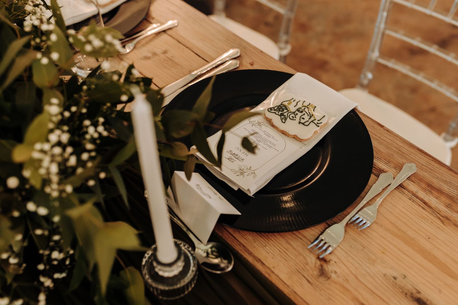 Rustic wedding place setting with black plates, candles and baby's breath on wooden table.