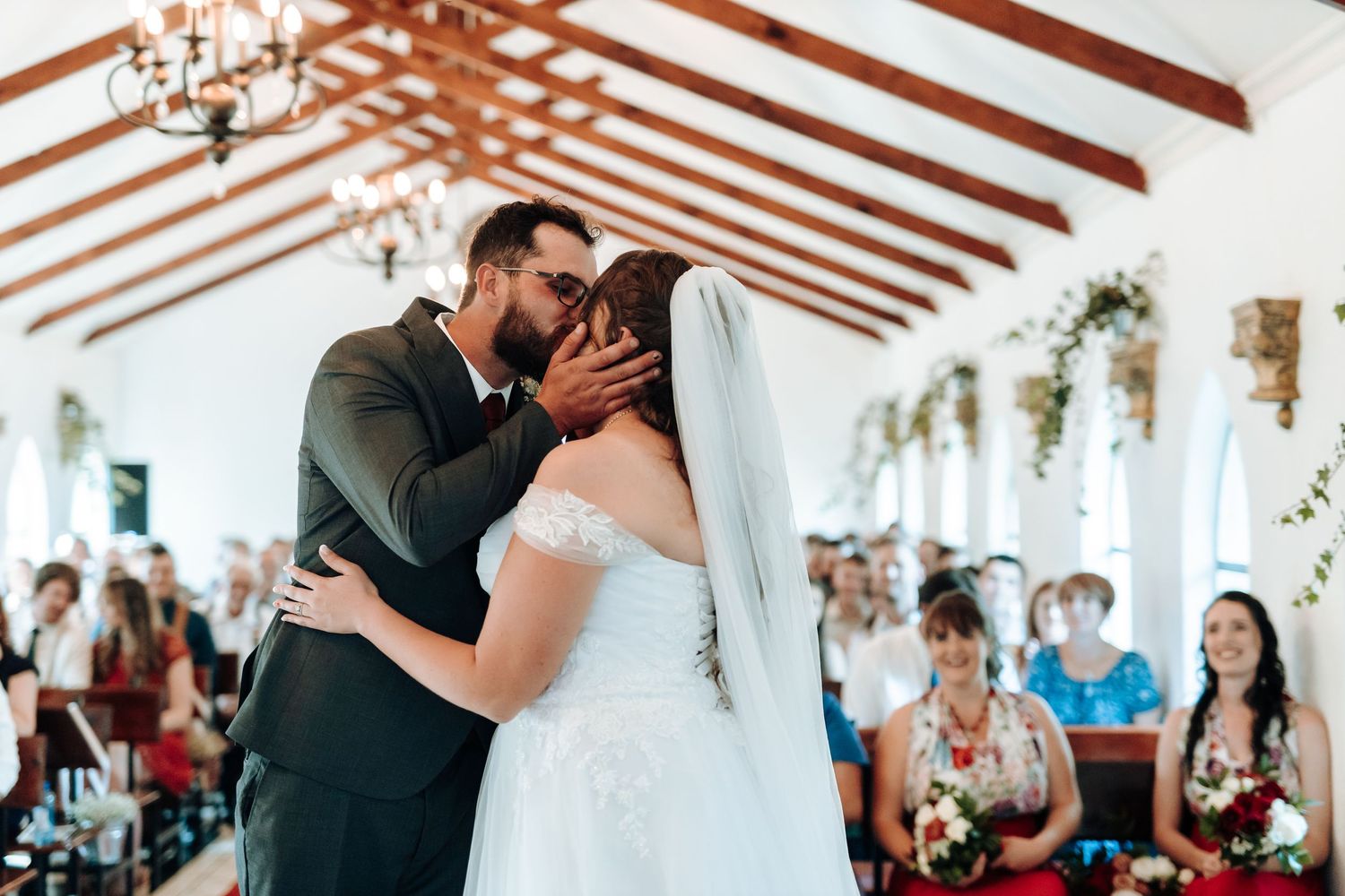 Romantic first kiss as newlyweds during chapel ceremony with guests watching.