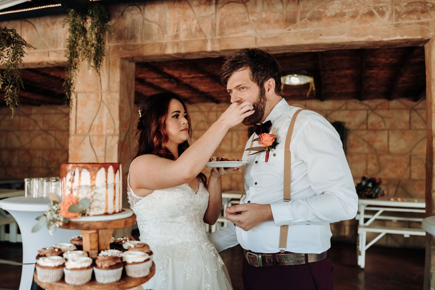 Bride and groom laughing while sharing cupcakes at their rustic-themed reception.
