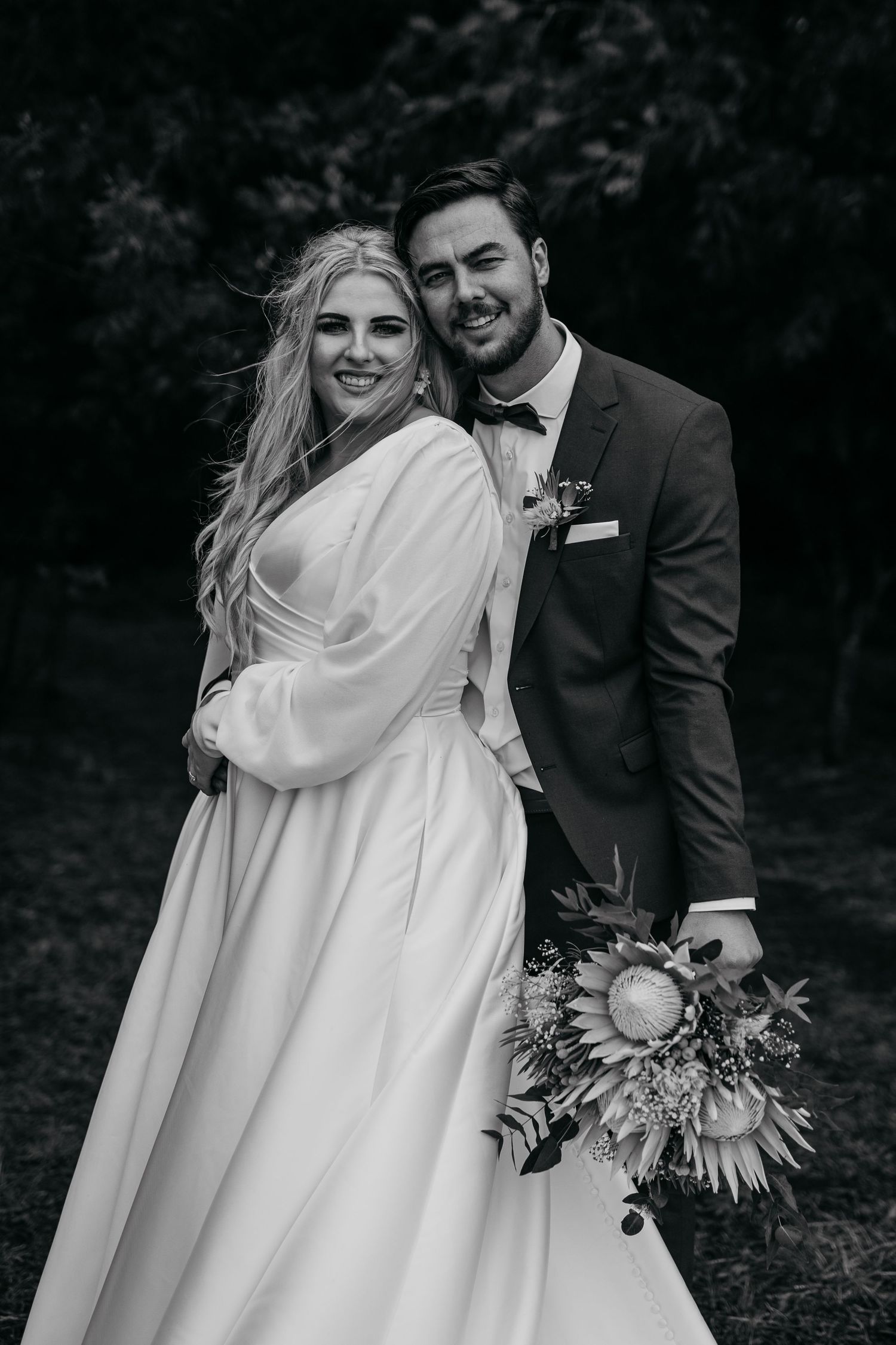 Black and white portrait of newlyweds with bride holding dramatic floral bouquet.