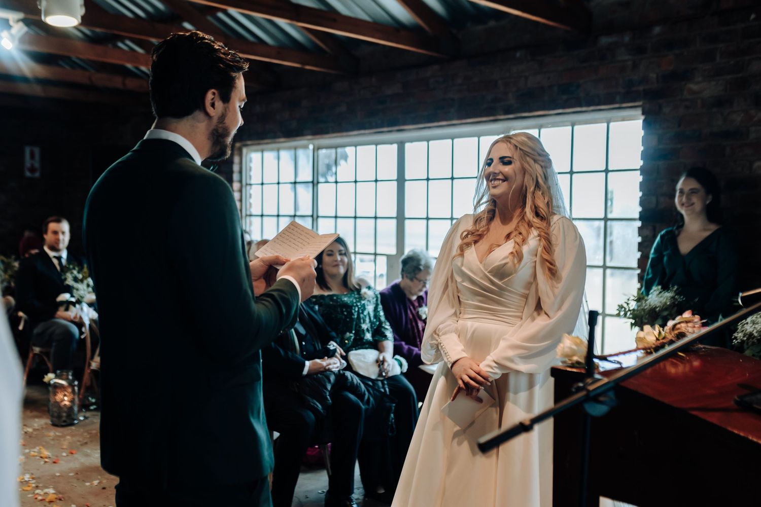 A classic wedding ceremony scene inside a rustic brick venue with natural light streaming through windows.