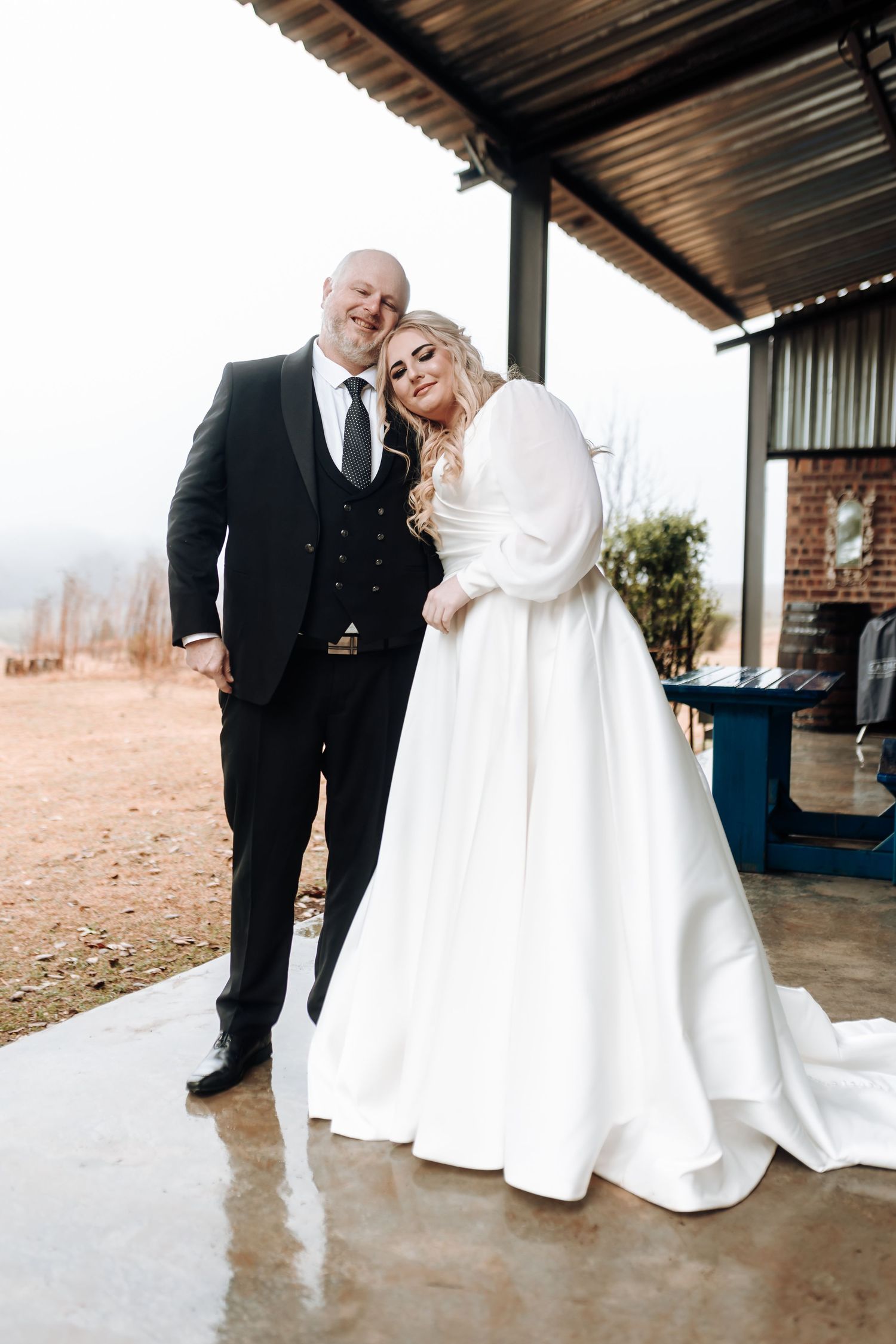 Elegant bride and groom embrace under covered porch during their winter wedding.