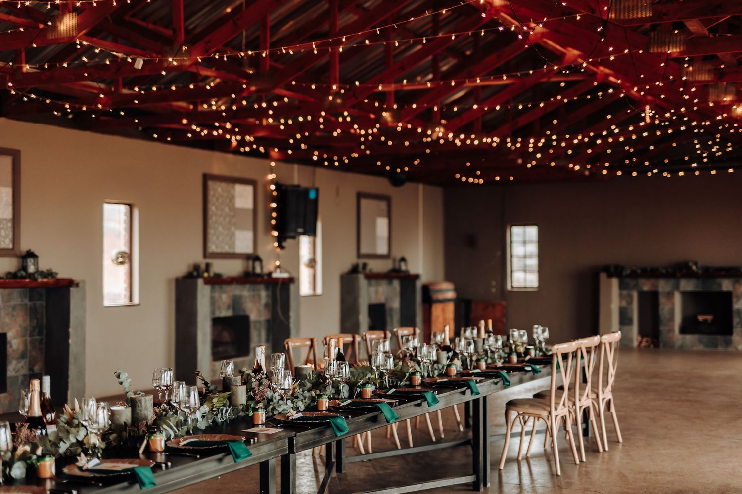 Wedding reception hall with hanging string lights and long tables set for dinner.