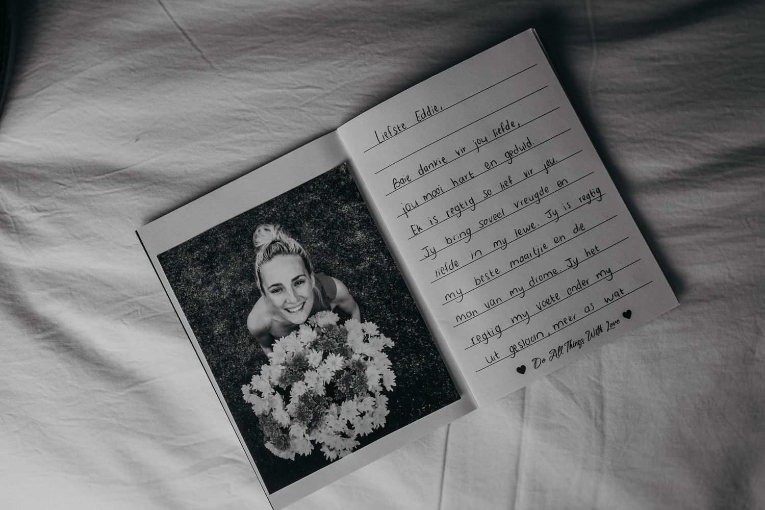 Black and white notebook with handwritten note and photograph lying on white fabric.