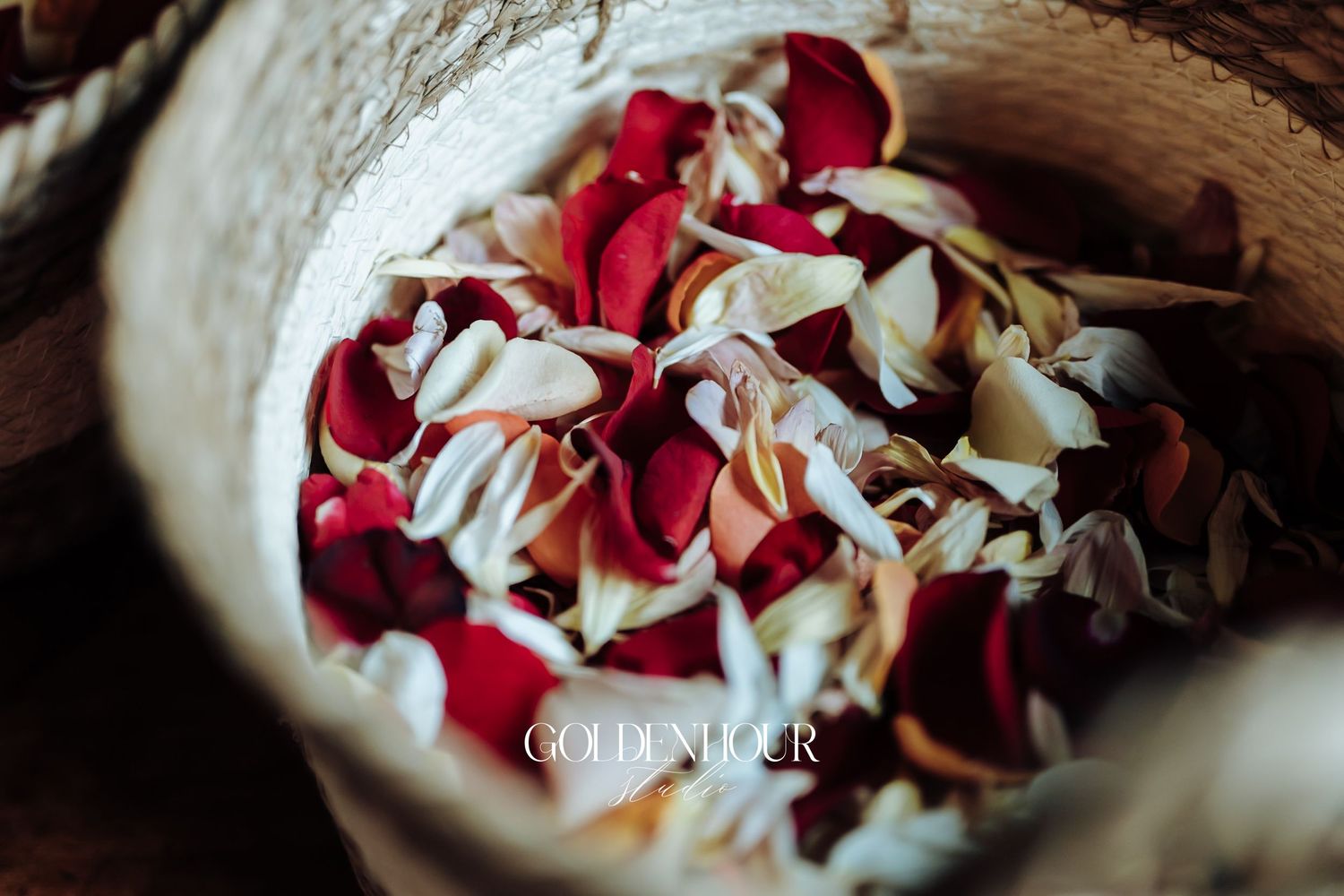 Close-up of red and white rose petals in a wooden bowl for wedding ceremony.