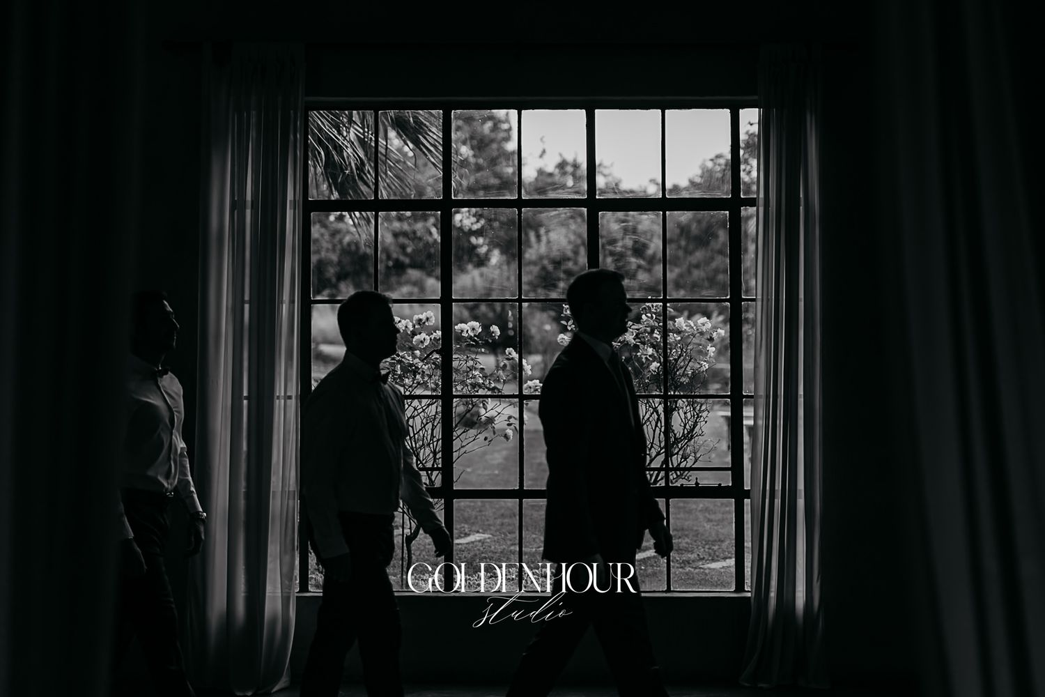 Silhouette of two men standing by a large window in black and white wedding photography.