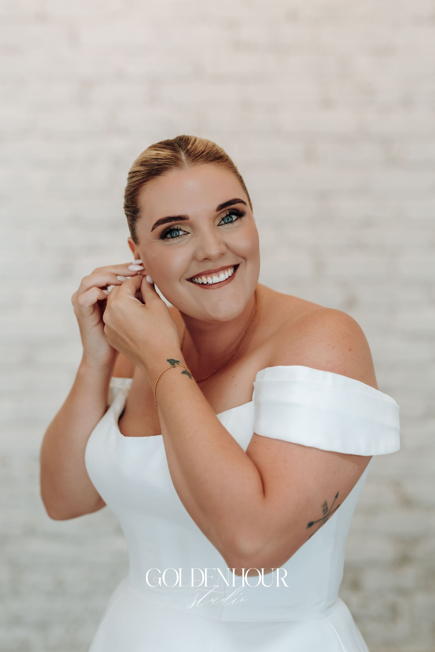 Bride in off-shoulder white wedding dress smiles radiantly in artistic bridal portrait series.