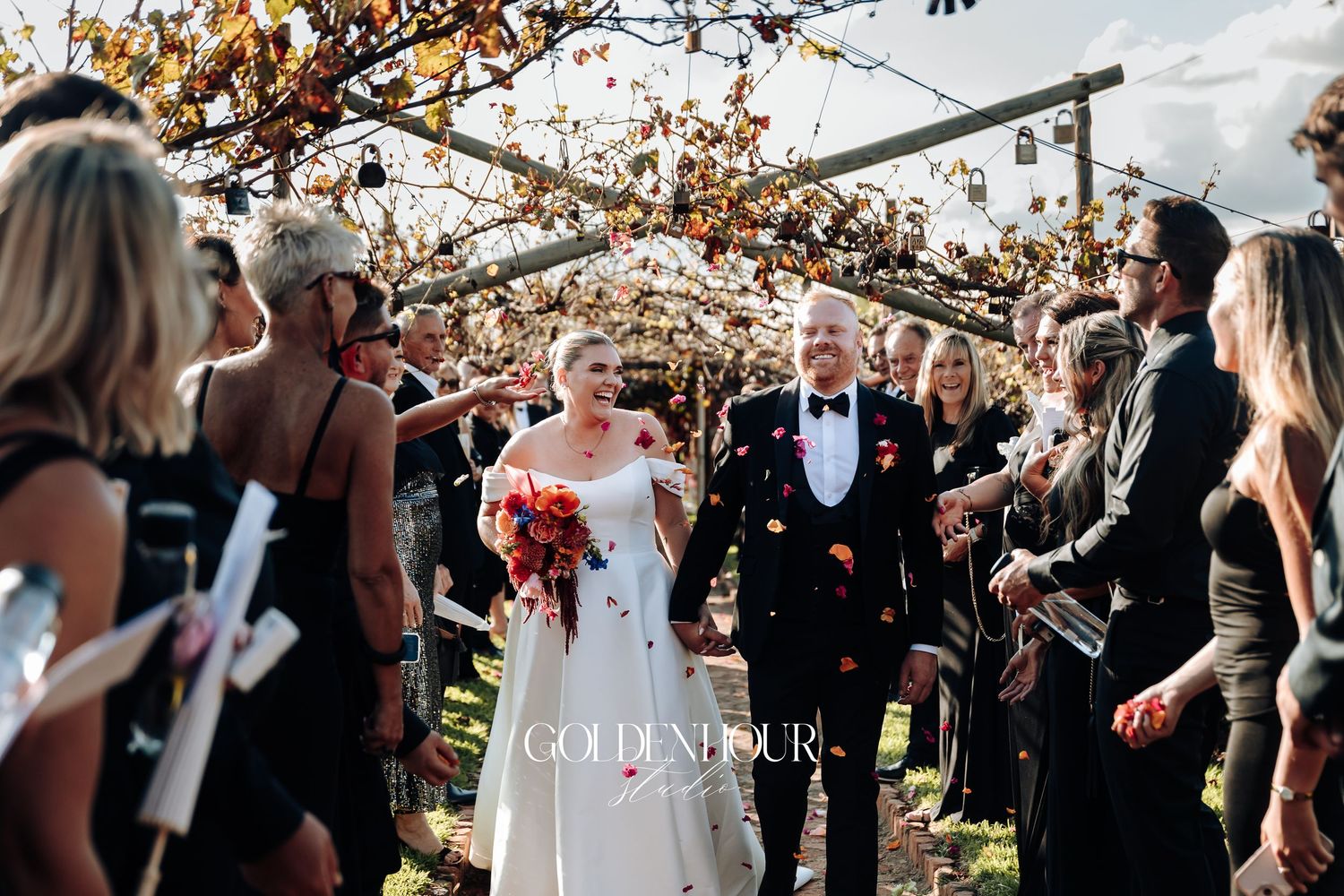 Wedding guests mingle and dance beneath rustic wooden beams decorated with string lights and floral arrangements.
